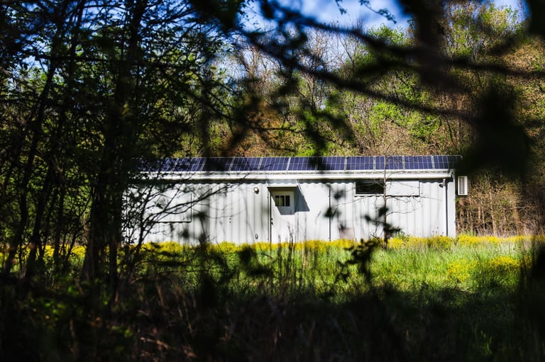 White trailer with solar panels on roof surrounded by trees and green grass field